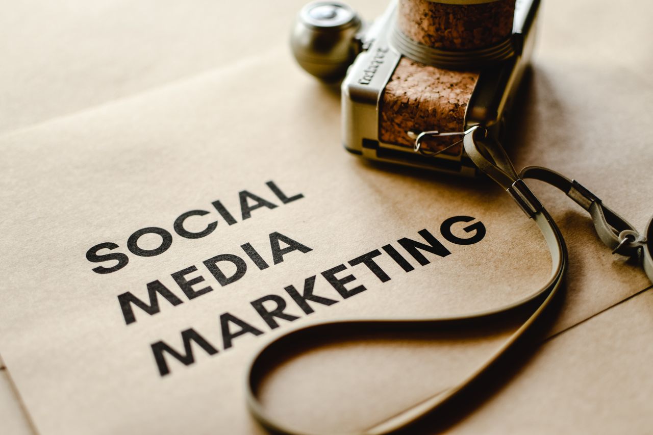 heros-img A close-up of a camera resting on brown paper with the words Social Media Marketing, highlighting digital marketing concepts.